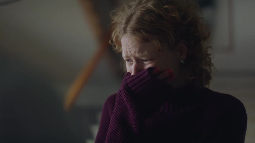 A woman in a room crying with a wall and staircase in the background