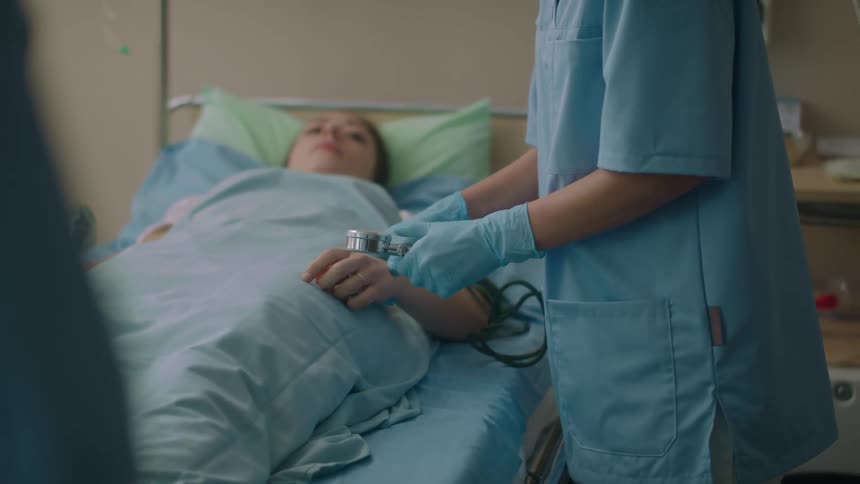 Nurse measures blood pressure on a patient laying over a hospital bed