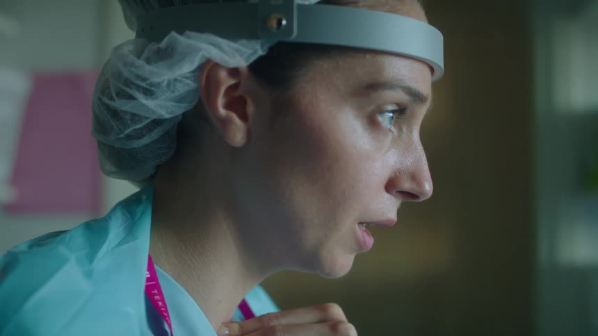 A woman doctor dressed in scrubs looks troubled as she hold her hand on her chest and takes deep breaths