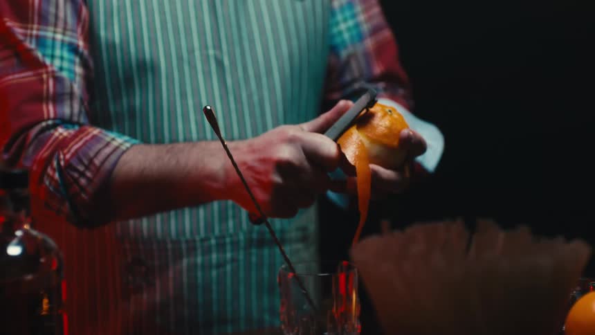 A man uses a peeler to peel an orange