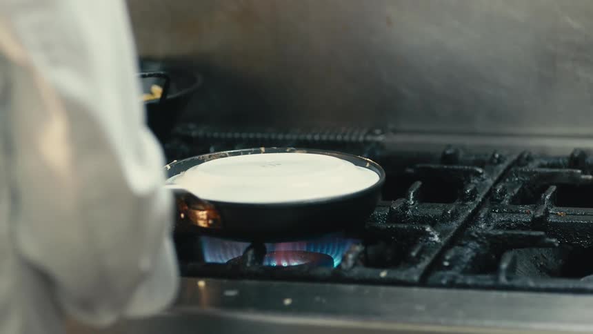Chef upends egg dish onto white plate from skillet after cooking it on gas stove