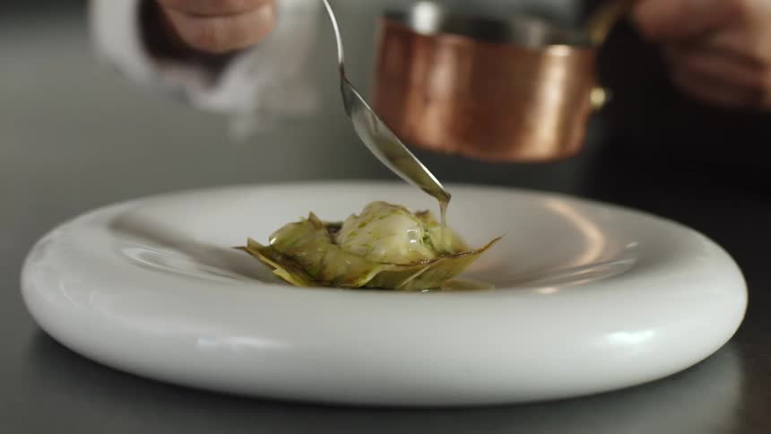 A person with a spoon adding sauce to a dish