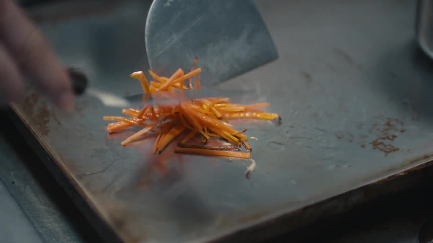 A person using their hands to spatula food slices on a grill
