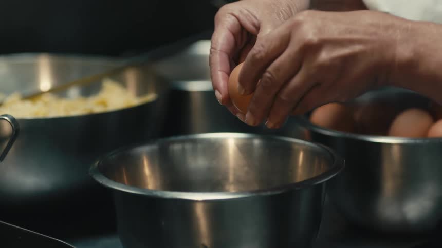 A chef is cracking a brown egg into a silver bowl