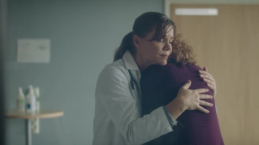 A woman doctor is talking to another woman and giving her a hug