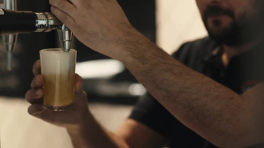 A man fills a glass with beer and it overspills