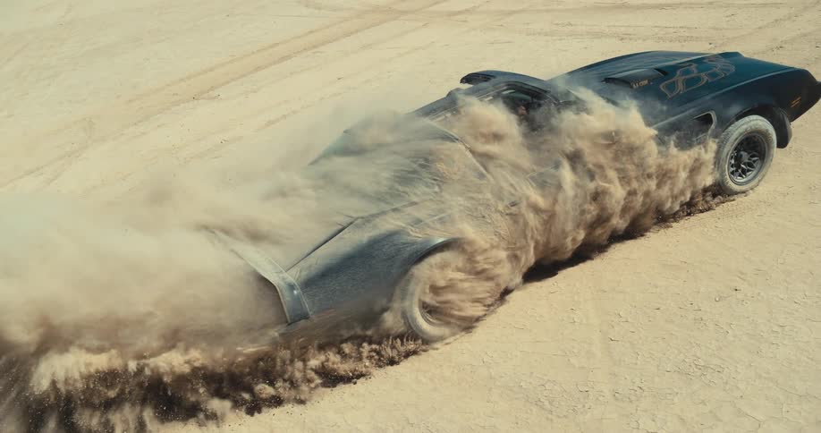 A black trans am with ttops is sliding across the desert and sand is flying