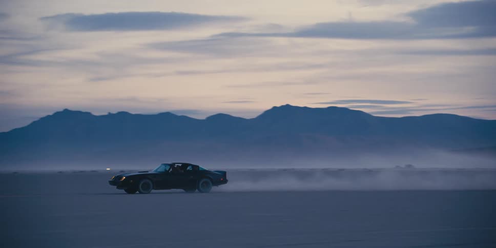 Black muscle car kicking dust on the desert near the mountains at sunset