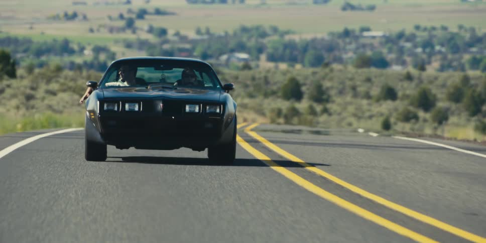 A man in the passenger seat with his hand out the window playing in the wind