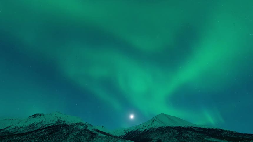 A time lapse of the aurora borealis in the sky above snow capped mountains