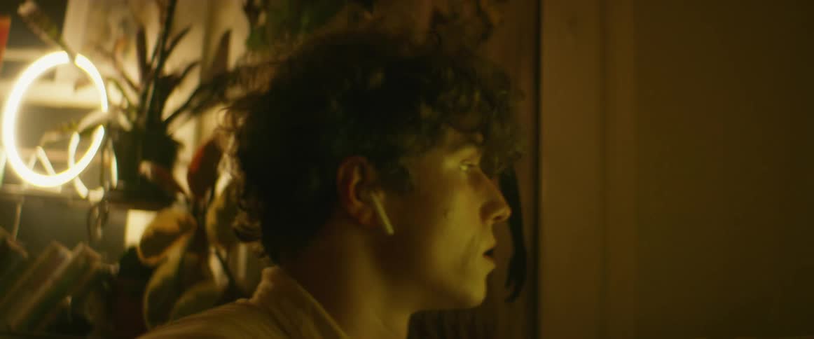 Young man wearing earbuds sitting on a dimly lit room at home