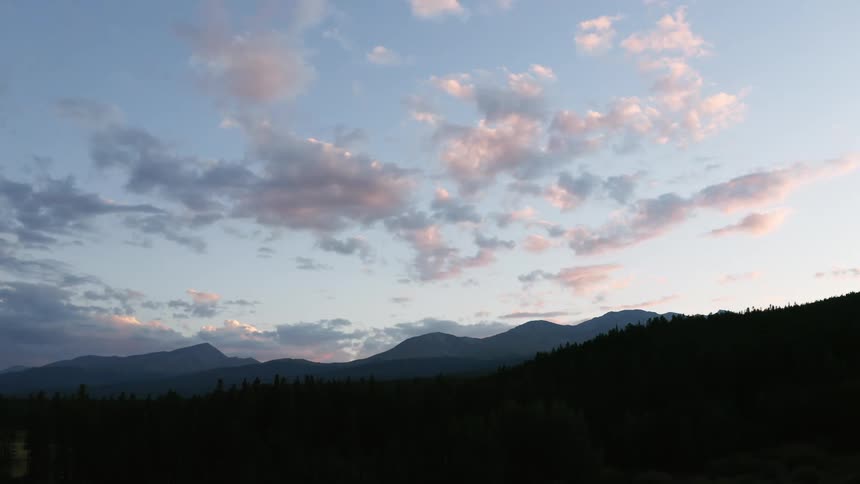 A forest with trees with a mountain range the sky and clouds in the background