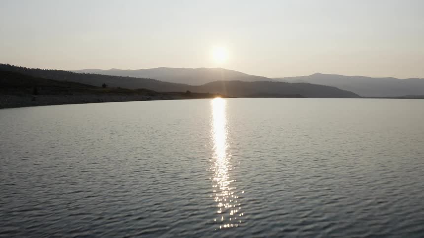 The sun sits low in the sky as it reflects off a lake in the mountains