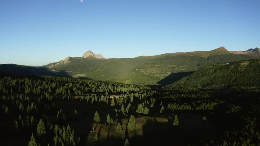 A landscape with trees and hills with a mountain range the sky and clouds in the background