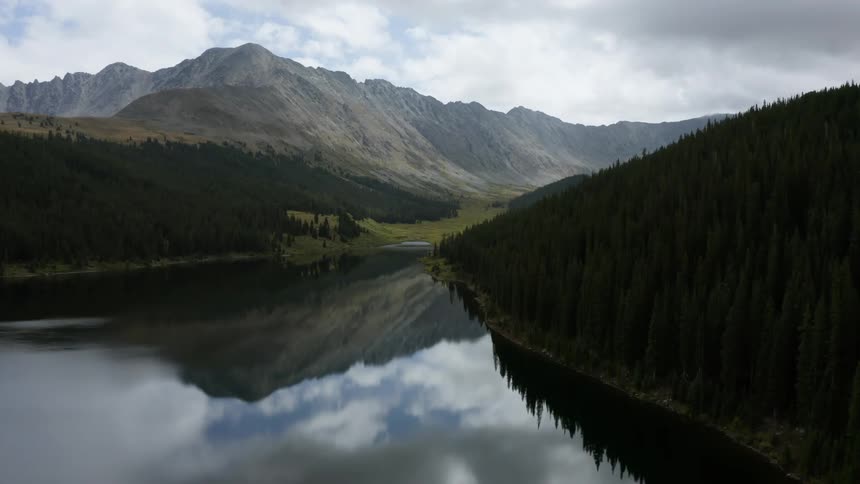 A glassy lake is still as mountains loom overhead