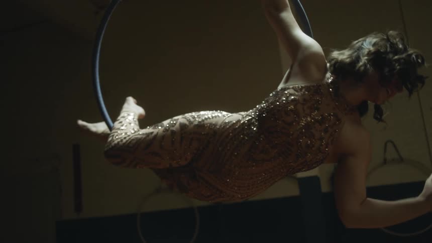 A woman smiles as she practices acrobatics while hanging on a ring