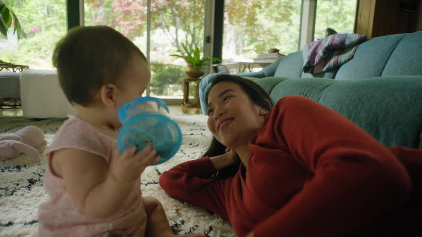 A mother is playing with her girl toddler on a rug in a living room during the daytime