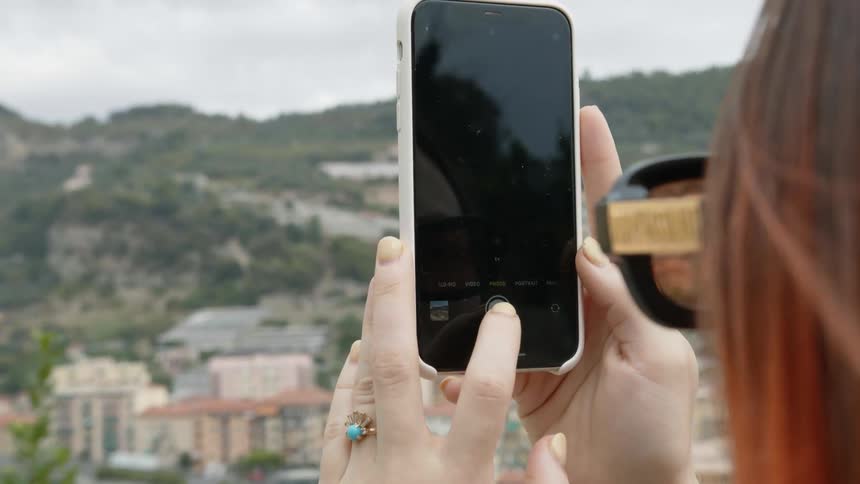 A woman uses her phone to take a photo of a neighborhood in the distance