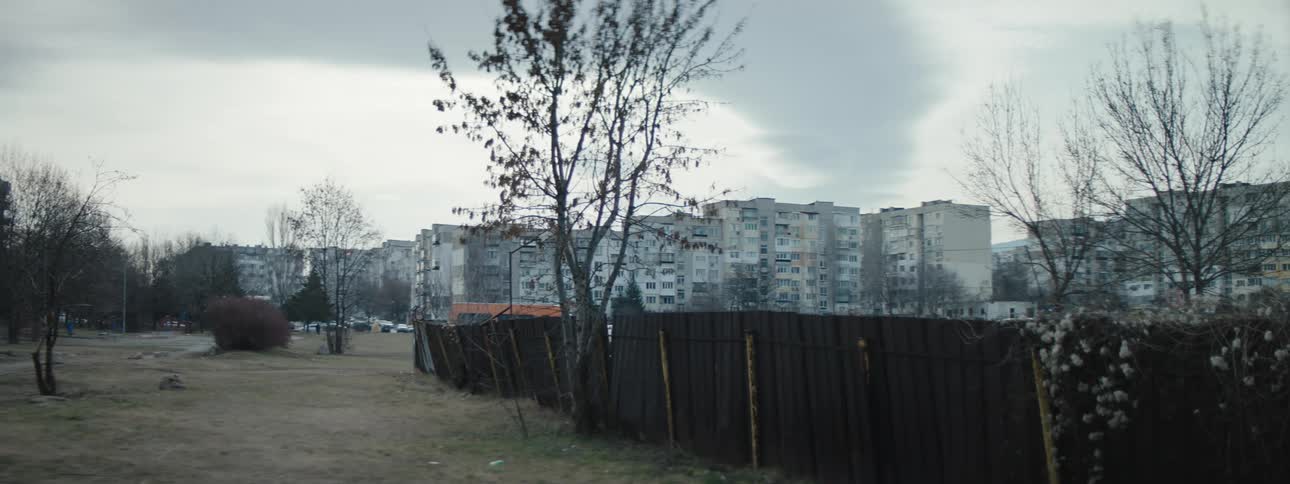 A partially falling fence surrounds a large apartment complex
