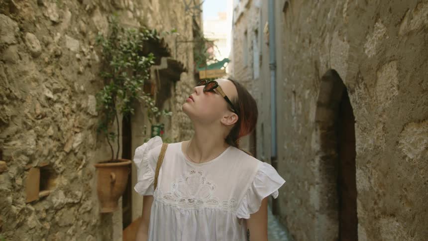 A woman looks over the stone buildings as she walks in the alley