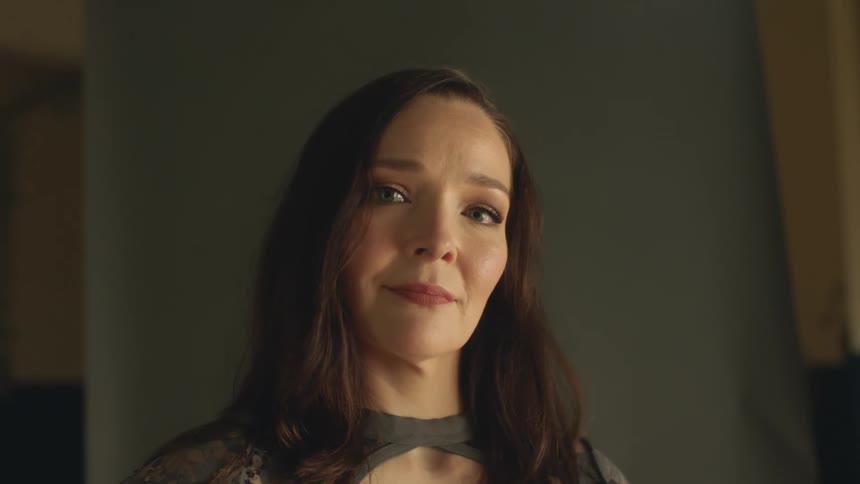 A woman is standing expressionless in a room