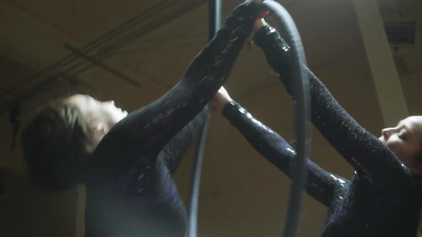 Two female dancers are in a dance studio practicing a routine involving a ring suspended from the ceiling