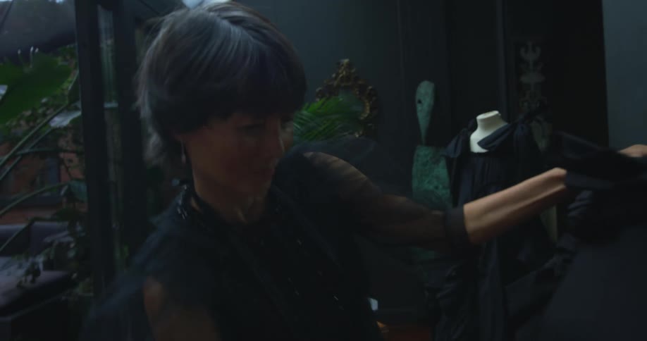 A female seamstress adjusting a black piece of clothing on a mannequin