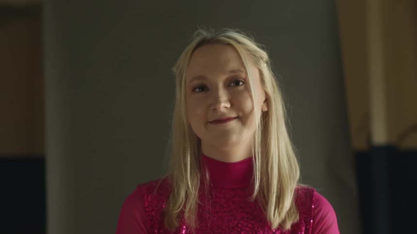A woman smiles and blinks a lot as she stands still in a room