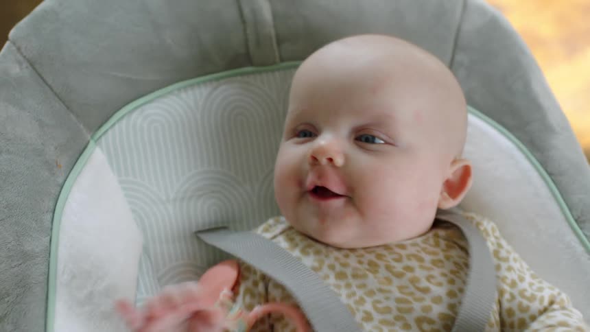 A young baby smiles and laughs as she sits in a bouncy seat