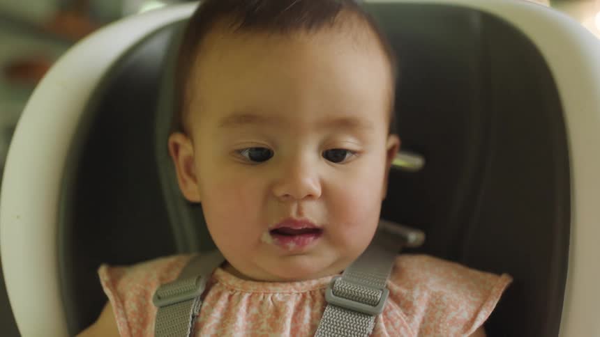 A baby opens her mouth wide while being fed in her highchair