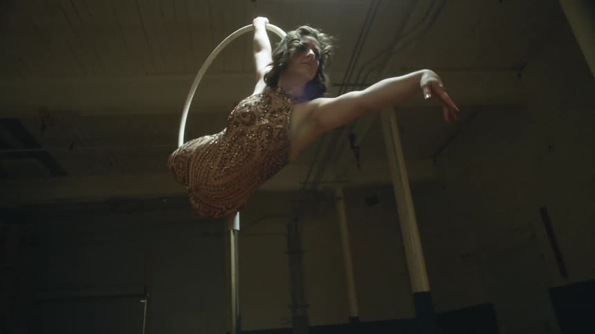 A woman wearing a sequin outfit is performing acrobatic movements on a pole