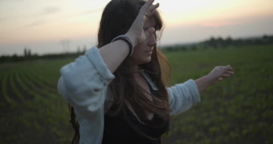 A woman is dancing with her eyes closed in a field