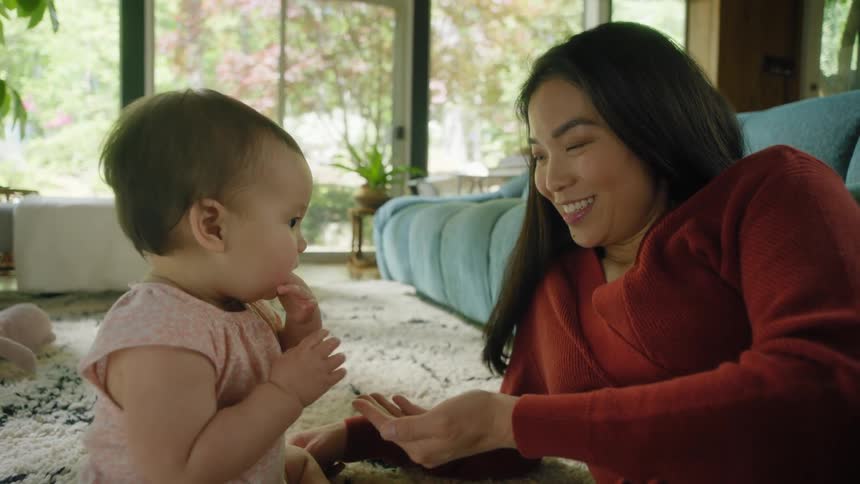 A mother smiling and interacting with her baby on a living room rug