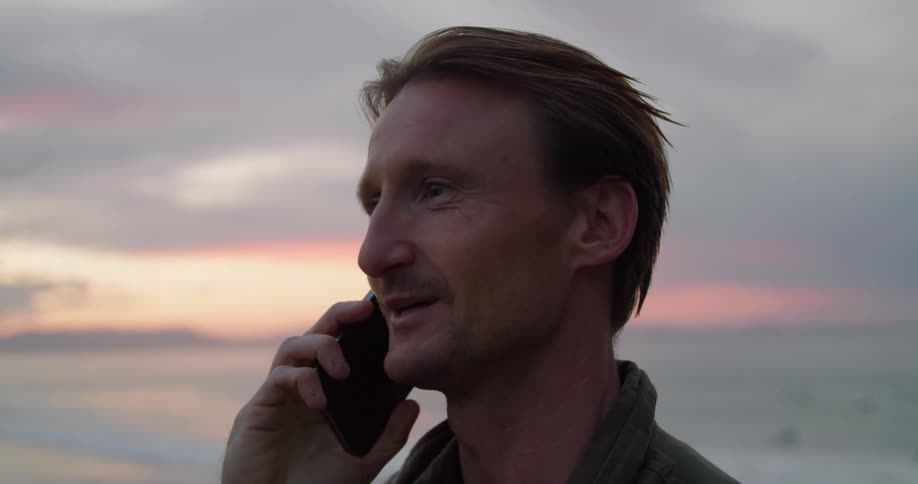 A man talks on his cell phone at sunset on the beach