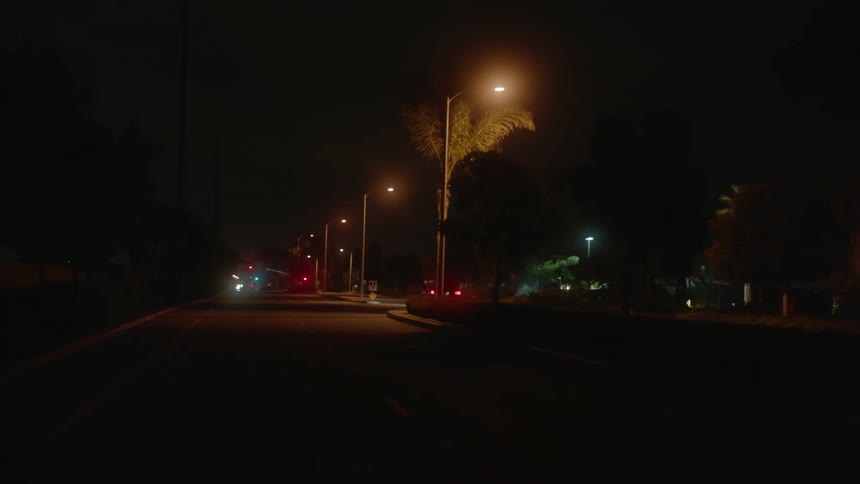 Cars travel on a road at night with headlights on and street lights lit