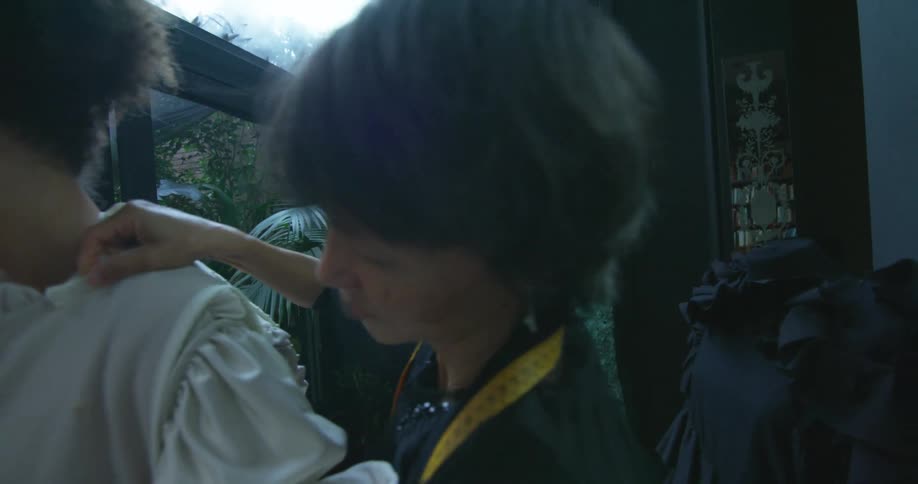 Clothing designer adjusts outfit on model standing in design studio