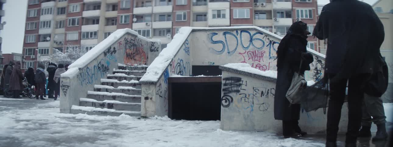 People standing on concrete with snow with stairs buildings the sky and clouds in the background