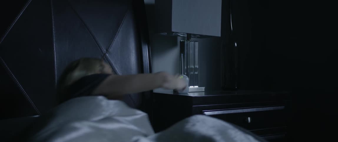 A woman wakes up and turns on the lamp by her bed