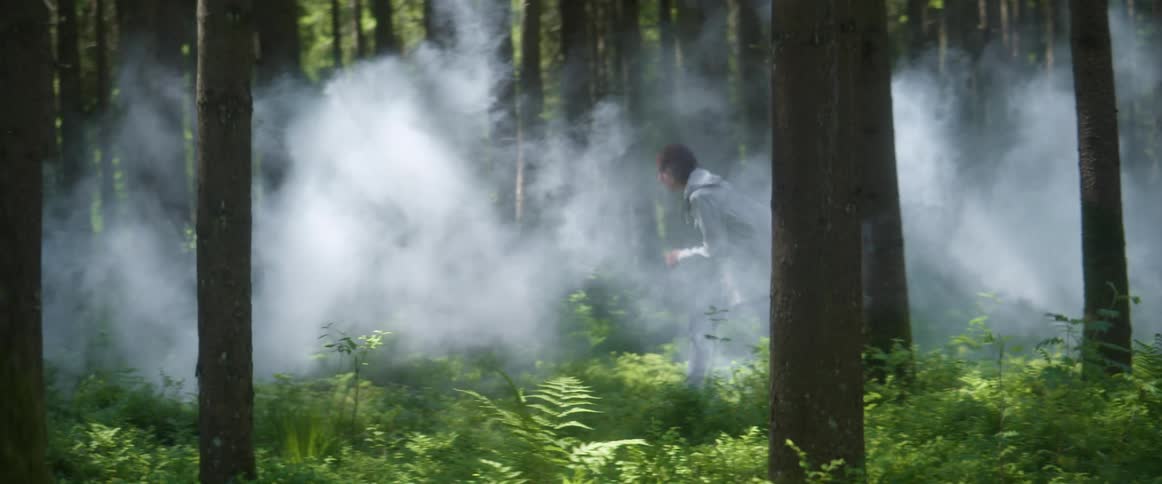 A young man is running through trees in a smoke filled forest