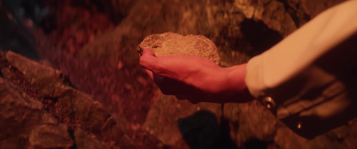 Man wearing long sleeves picks up rock from ground under and artificial light