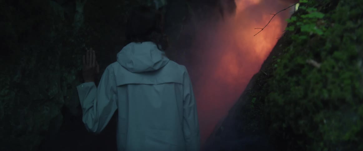 A teenage boy walks between two cliffs towards a fire