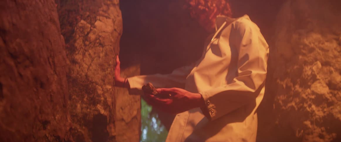 Someone is standing inside a dark cave and they pick up a rock from the wall and the inside of the cave lights up