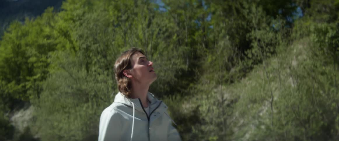 A young man is hiking in the wilderness near trees and mountains on sunny day