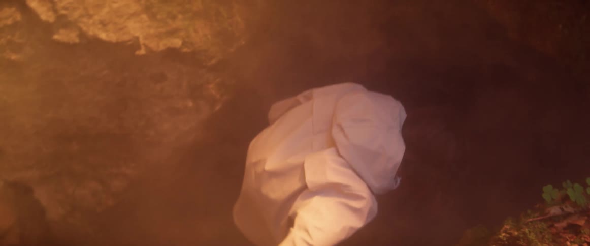 A man crawls down into the dark cave