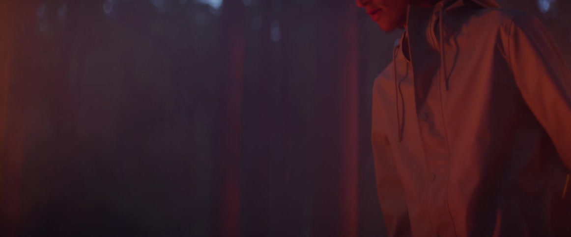 A man in the forest is staring down at a nearby fire at dusk