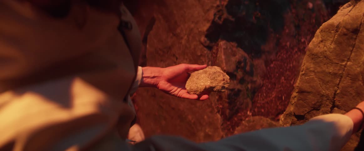 A person outdoors picks up a rock and throws it back on the ground after looking at it