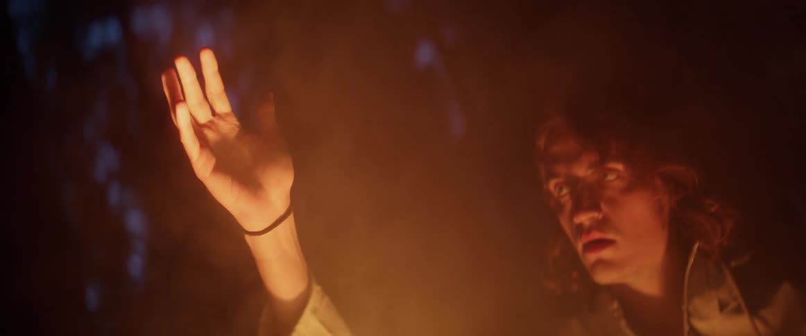 A man stares at his hand as he runs through smoke from a campfire in the forest