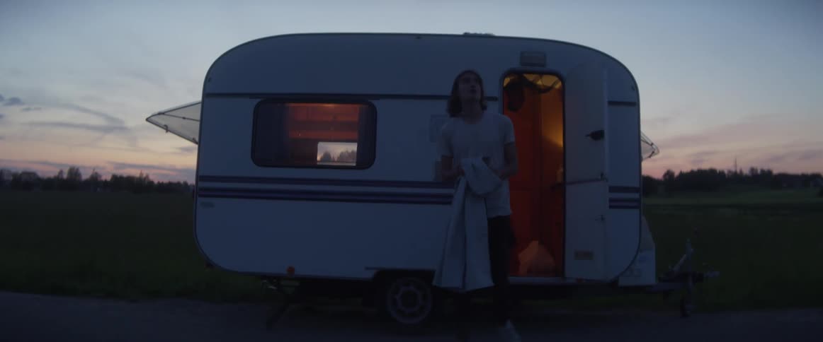 A man walking out of a camper with a grassy field trees the sky and clouds in the background