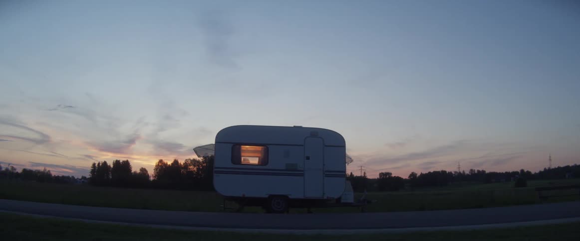 A mini trailer is sitting on the side of a road in an empty field at dusk