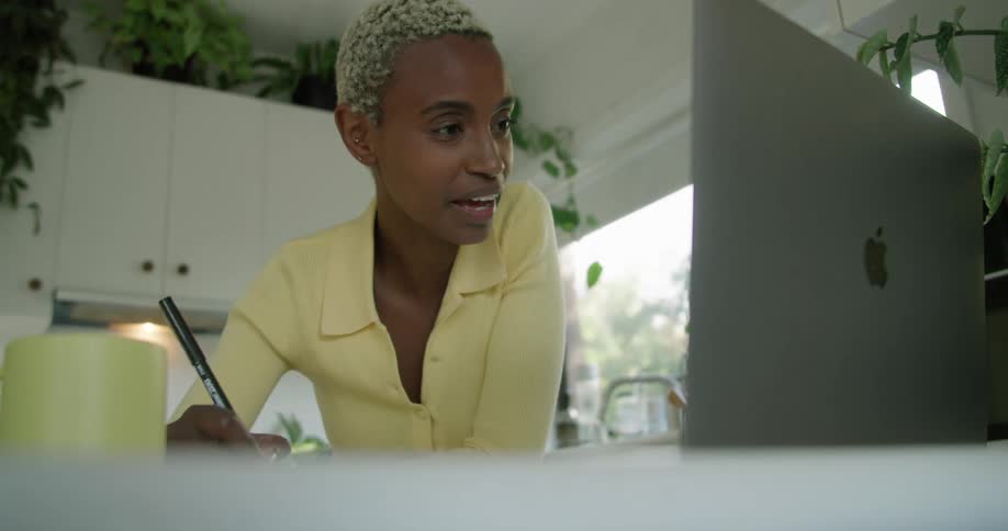 A woman talks on the laptop while taking notes